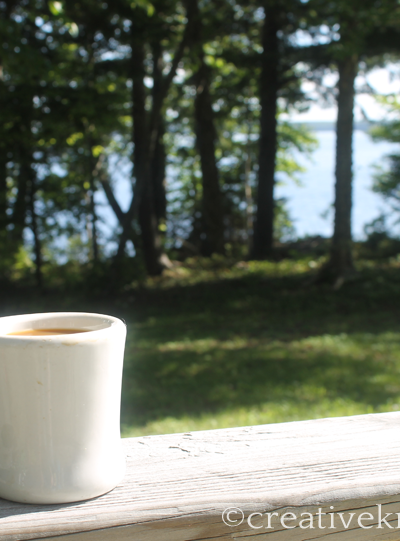Coffee mug on wooden railing overlooking trees and water